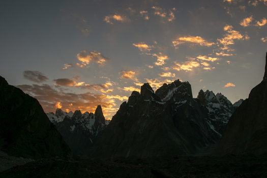 View of the jagged granite spires of the Trango Towers at sunset with golden light illuminating the clouds above the Karakoram mountain range in Pakistan. View of the jagged granite spires of the Trango Towers at sunset with golden light illuminating the clouds above the Karakoram mountain range in Pakistan.