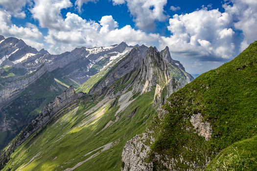 Aerial view of jagged peaks rise majestically their rocky faces contrasting with the vibrant green slopes under a sky streaked with clouds Schwende Rüte Appenzell Innerrhoden Switzerland. Aerial view of jagged peaks rise majestically their rocky faces contrasting with the vibrant green slopes under a sky streaked with clouds Schwende Rüte Appenzell Innerrhoden Switzerland.