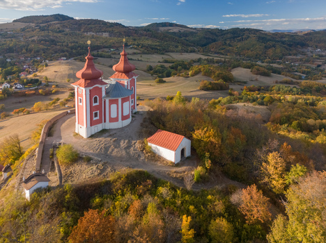Aerial view of the historic Stiavnicka Kalvaria pilgrimage site with its red and white church surrounded by autumn forests and hills in Banska Stiavnica Banskobystricky kraj Slovakia. Aerial view of the historic Stiavnicka Kalvaria pilgrimage site with its red and white church surrounded by autumn forests and hills in Banska Stiavnica Banskobystricky kraj Slovakia.