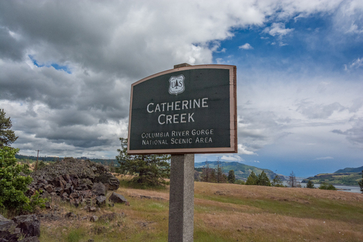 View of the Catherine Creek sign in the Columbia River Gorge National Scenic Area with rocky terrain and a cloudy sky in Hood River Oregon United States.