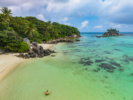 Aerial view of the sun kissed beach where turquoise waters meet the shore near verdant trees and scattered rock formations Anse Royale Mahe Island Seychelles. Aerial view of the sun kissed beach where turquoise waters meet the shore near verdant trees and scattered rock formations Anse Royale Mahe Island Seychelles.