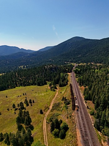 Aerial view of a freight train traveling along tracks through a dense pine forest and mountainous landscape near Golden Colorado United States. Aerial view of a freight train traveling along tracks through a dense pine forest and mountainous landscape near Golden Colorado United States.