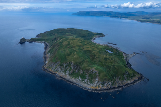 Aerial view of Sanda Island near the Mull of Kintyre featuring rugged green terrain rocky cliffs a lighthouse and surrounding deep blue waters Argyll and Bute Scotland United Kingdom.