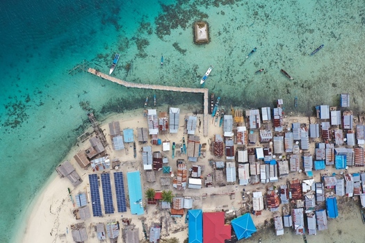Aerial view of Pulau Maginti featuring traditional stilt houses a wooden pier extending into turquoise waters solar panels and small boats in Maginti South East Sulawesi Indonesia.