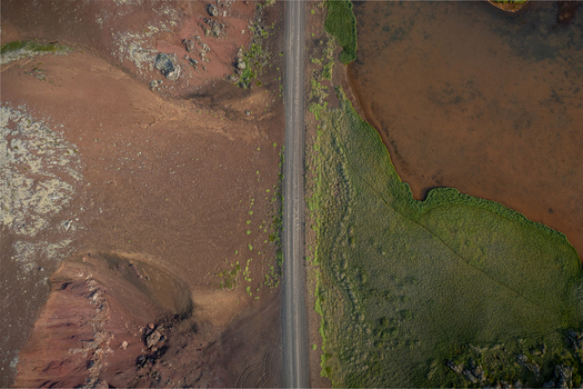 Aerial view of Ytri Raudarmelskula volcanic crater with a road cutting through the rugged reddish brown volcanic landscape and green mossy terrain in Raudhamelur Eyja og Miklaholtshr Iceland. Aerial view of Ytri Raudarmelskula volcanic crater with a road cutting through the rugged reddish brown volcanic landscape and green mossy terrain in Raudhamelur Eyja og Miklaholtshr Iceland.