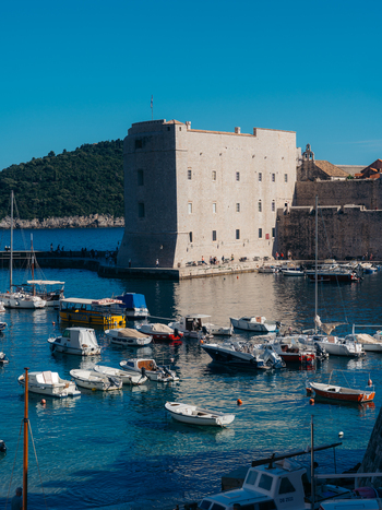 View of St. John s Fortress and the old harbor with small boats moored in clear blue water in Dubrovnik Dubrovnik Neretva County Croatia. View of St. John s Fortress and the old harbor with small boats moored in clear blue water in Dubrovnik Dubrovnik Neretva County Croatia.