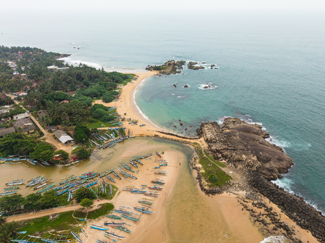 Aerial view of traditional fishing boats parked on a sandy beach near rocky outcrops and turquoise ocean water in Dodanduwa Southern Province Sri Lanka. Aerial view of traditional fishing boats parked on a sandy beach near rocky outcrops and turquoise ocean water in Dodanduwa Southern Province Sri Lanka.
