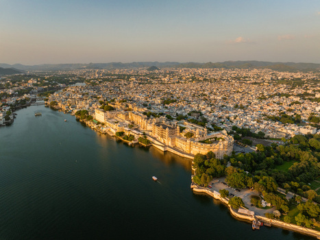 Aerial view of the historic City Palace complex situated on the banks of Lake Pichola surrounded by the urban landscape of Udaipur Rajasthan India.