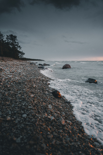 View of Saxby rannik featuring a rocky shoreline with waves crashing against stones under a dramatic dark cloudy sky at sunset in Saxby Laane maakond Estonia.