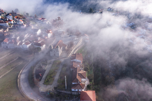 Aerial view of the historic village of Avo with its church and red tiled houses partially shrouded in thick morning fog Oliveira do Hospital Coimbra District Portugal.