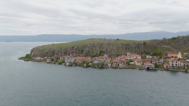 Aerial view of the village of Lin featuring red roofed houses along the rocky shoreline of Lake Ohrid under a cloudy sky in Lin Korce County Albania. Aerial view of the village of Lin featuring red roofed houses along the rocky shoreline of Lake Ohrid under a cloudy sky in Lin Korce County Albania.