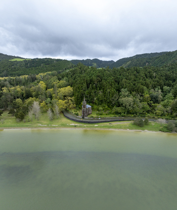 Aerial view of Ermida de Nossa Senhora das Vitorias situated on the shore of Furnas Lake surrounded by lush green hills and forest in Furnas Acores Portugal. Aerial view of Ermida de Nossa Senhora das Vitorias situated on the shore of Furnas Lake surrounded by lush green hills and forest in Furnas Acores Portugal.