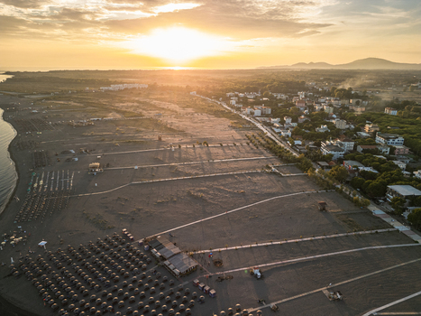 Aerial view of Velipoja Beach at sunset with sandy coastline rows of beach umbrellas and coastal town buildings in Velipoje Shkoder County Albania.