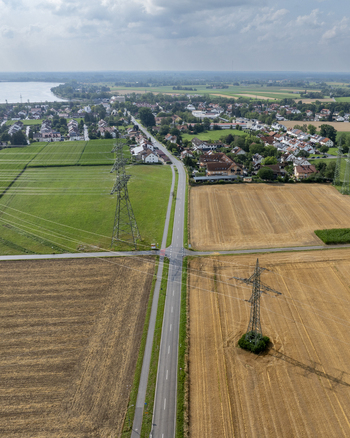 Aerial view of Neufinsing with a road cutting through agricultural fields and power lines under a blue sky in Finsing Bayern Germany.