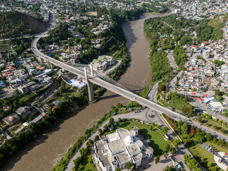 Aerial view of a modern concrete bridge spanning a wide river with urban buildings and lush green trees in Muzaffarabad Azad Kashmir Pakistan. Aerial view of a modern concrete bridge spanning a wide river with urban buildings and lush green trees in Muzaffarabad Azad Kashmir Pakistan.