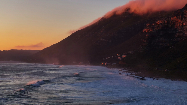Aerial view of the rugged coastline with waves crashing against the shore and clouds rolling over the mountain peaks during sunset in Cape Town Western Cape South Africa. Aerial view of the rugged coastline with waves crashing against the shore and clouds rolling over the mountain peaks during sunset in Cape Town Western Cape South Africa.