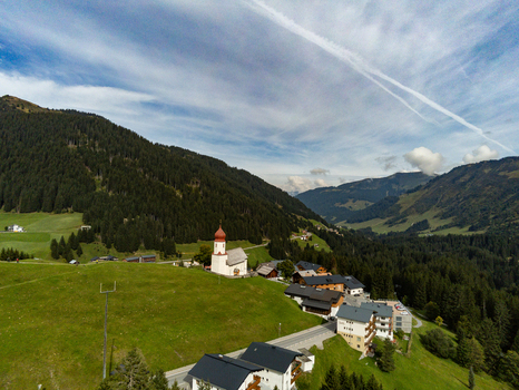 Aerial view of Oberdamuls village and its iconic church nestled in the green mountains of the Austrian Alps surrounded by lush meadows and pine forests in Oberdamuls Vorarlberg Austria.