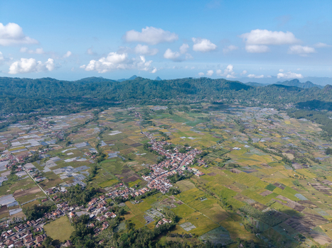Aerial view of the village of Sumberurip nestled among lush green rice paddies and agricultural fields in the mountainous region of Pronojiwo East Java Indonesia. Aerial view of the village of Sumberurip nestled among lush green rice paddies and agricultural fields in the mountainous region of Pronojiwo East Java Indonesia.