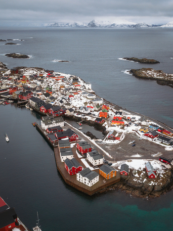 Aerial view of vibrant red and white buildings dot the snow dusted landscape juxtaposed against the dark icy waters surrounding the small island Henningsv&aelig;r Nordland Norway.