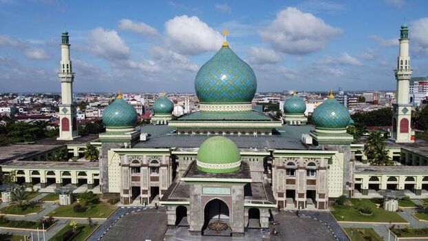 Aerial view of An Nur Great Mosque with its distinctive green domes and minarets set against the urban skyline of Pekanbaru Riau Indonesia.
