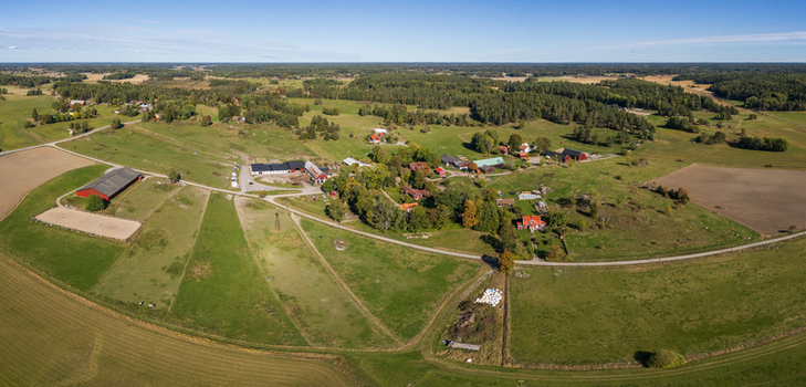Aerial view of traditional red wooden farmhouses surrounded by sprawling green pastures agricultural fields and forests in the Swedish countryside in Rimbo Stockholm County Sweden.