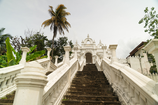View of the ornate white entrance and stone staircase of a Buddhist temple surrounded by palm trees under an overcast sky in Dodanduwa Southern Province Sri Lanka. View of the ornate white entrance and stone staircase of a Buddhist temple surrounded by palm trees under an overcast sky in Dodanduwa Southern Province Sri Lanka.