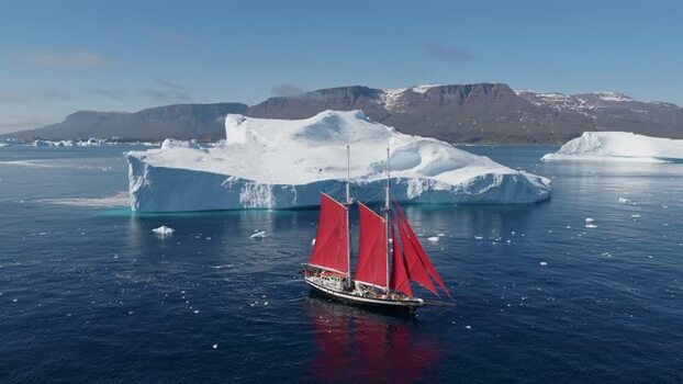 Aerial view of sailboat with red sails near iceberg Greenland. Aerial view of sailboat with red sails near iceberg Greenland.