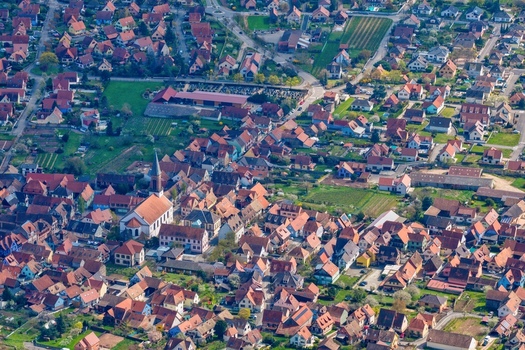Aerial view of terracotta roofs contrasting with verdant gardens the steeple of the church piercing the skyline Kintzheim Grand Est France.
