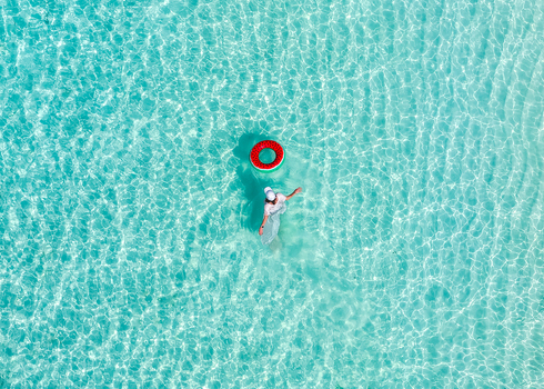Aerial view of a woman wading in crystal clear turquoise water next to a red inflatable ring in Vashafaru Haa Alif Atoll Maldives. Aerial view of a woman wading in crystal clear turquoise water next to a red inflatable ring in Vashafaru Haa Alif Atoll Maldives.