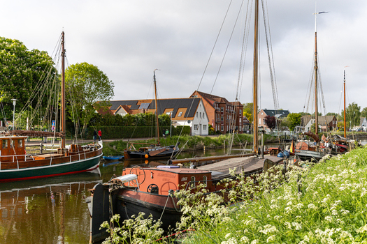 View of traditional sailing boats moored at Hafen Harlesiel with historic brick houses and lush greenery Wittmund Lower Saxony Germany. View of traditional sailing boats moored at Hafen Harlesiel with historic brick houses and lush greenery Wittmund Lower Saxony Germany.