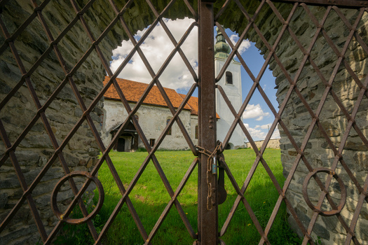 View of the historic Lutheran church through a rusty metal lattice gate with stone walls and a green lawn under a blue sky Rimavska Bana Banska Bystrica Region Slovakia. View of the historic Lutheran church through a rusty metal lattice gate with stone walls and a green lawn under a blue sky Rimavska Bana Banska Bystrica Region Slovakia.