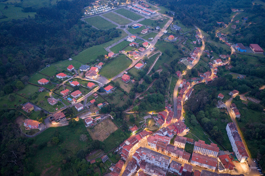 Aerial view of the illuminated houses and winding streets of the coastal town nestled among lush green hills at dusk Cudillero Asturias Spain. Aerial view of the illuminated houses and winding streets of the coastal town nestled among lush green hills at dusk Cudillero Asturias Spain.