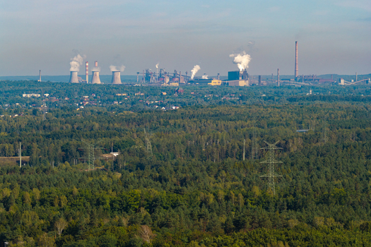 Aerial view of a large coal power plant with cooling towers and chimneys emitting smoke situated near a dense forest and urban area in Katowice Silesian Voivodeship Poland.
