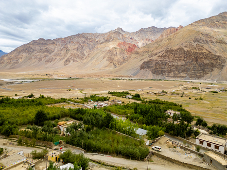Aerial view of the Zanskar Valley featuring lush green trees small village settlements and rugged mountain ranges under a cloudy sky in Zanskar Ladakh India.