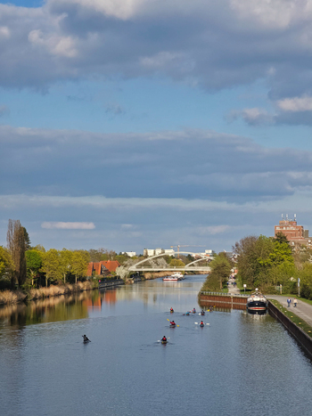 Hannover Germany 14 April 2026 View of kayakers paddling on the canal with a modern bridge in the background surrounded by lush green trees under a cloudy blue sky.