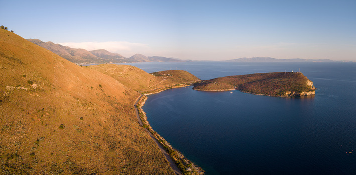 Aerial view of the rugged coastline and the Porto Palermo peninsula with a winding road along the arid hills and the deep blue sea in Porto Palermo Qarku i Vlores Albania. Aerial view of the rugged coastline and the Porto Palermo peninsula with a winding road along the arid hills and the deep blue sea in Porto Palermo Qarku i Vlores Albania.