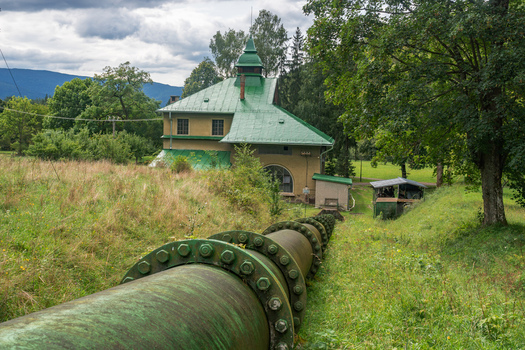 View of the historic Jasenie Hydroelectric Power Plant with its green roof and large industrial pipeline extending through the grassy landscape in Jasenie Banska Bystrica Regio Slovakia.