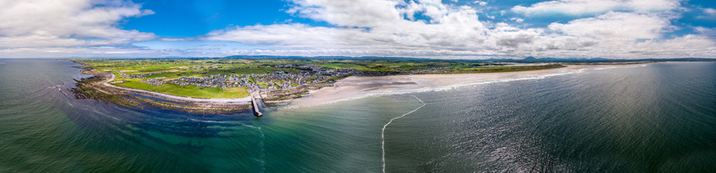 Aerial view of Enniscrone Pier and the surrounding sandy beach coastal town and green fields along the Atlantic Ocean in Enniscrone County Sligo Ireland.