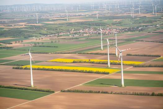 Aerial view of wind turbines standing in vast agricultural fields with yellow rapeseed flowers and a small village under a hazy sky Lower Austria Austria. Aerial view of wind turbines standing in vast agricultural fields with yellow rapeseed flowers and a small village under a hazy sky Lower Austria Austria.