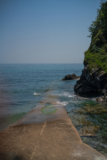 View of a concrete slipway extending into the calm sea beside a rocky cliff in Charlestown Cornwall United Kingdom. View of a concrete slipway extending into the calm sea beside a rocky cliff in Charlestown Cornwall United Kingdom.