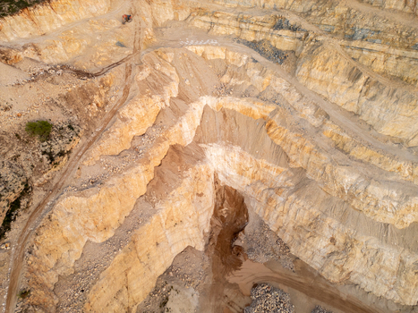 Aerial view of an open pit stone quarry with terraced rock walls dirt access roads and piles of excavated gravel in Teulada Valencian Community Spain.