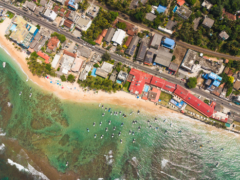 Aerial view of the turquoise coastline and sandy beach with small boats anchored near the shore and buildings along the road in Hikkaduwa Southern Province Sri Lanka. Aerial view of the turquoise coastline and sandy beach with small boats anchored near the shore and buildings along the road in Hikkaduwa Southern Province Sri Lanka.