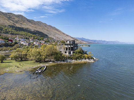 Aerial view of an abandoned building on the shore of Lake Shkodra with a sunken boat in the foreground and the village of Shiroka in the background Shiroka Shkoder County Albania. Aerial view of an abandoned building on the shore of Lake Shkodra with a sunken boat in the foreground and the village of Shiroka in the background Shiroka Shkoder County Albania.
