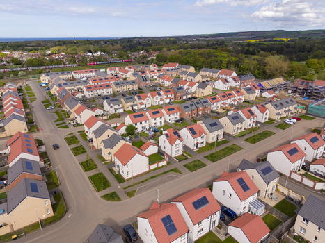 Aerial view of a modern residential housing estate with red roofed houses featuring solar panels and green gardens Edinburgh Scotland United Kingdom.