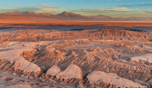 Aerial view of Valley of the Moon with rugged rock formations salt crusted terrain and distant volcanic mountains under a clear sky at sunset in San Pedro de Atacama Antofagasta Chile.