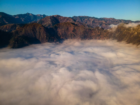 Aerial view of thick white clouds filling a valley surrounded by rugged mountain peaks under a clear blue sky Muzaffarabad Azad Kashmir Pakistan. Aerial view of thick white clouds filling a valley surrounded by rugged mountain peaks under a clear blue sky Muzaffarabad Azad Kashmir Pakistan.