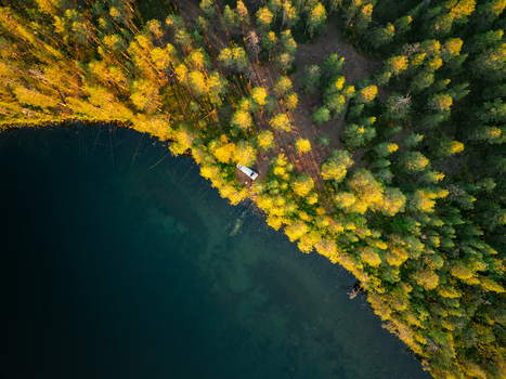Aerial view of a campervan parked on the edge of a deep blue lake surrounded by a dense pine forest in Sweden. Aerial view of a campervan parked on the edge of a deep blue lake surrounded by a dense pine forest in Sweden.