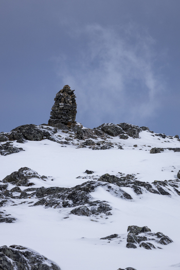 View of a stone cairn standing on a snowy mountain ridge under a cloudy sky in the arctic landscape of Kvaloya Troms Norway.