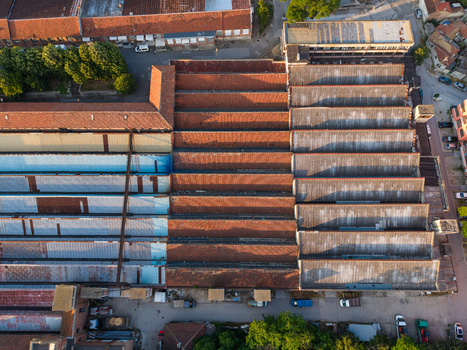 Aerial view of an industrial building with a distinctive sawtooth roof featuring rows of weathered tiles and metal sections surrounded by urban infrastructure in Varna Varna Bulgaria. Aerial view of an industrial building with a distinctive sawtooth roof featuring rows of weathered tiles and metal sections surrounded by urban infrastructure in Varna Varna Bulgaria.