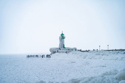 View of Molenfeuer Sassnitz covered in ice on a frozen pier with people walking along the icy breakwater in Sassnitz Mecklenburg Vorpommern Germany.